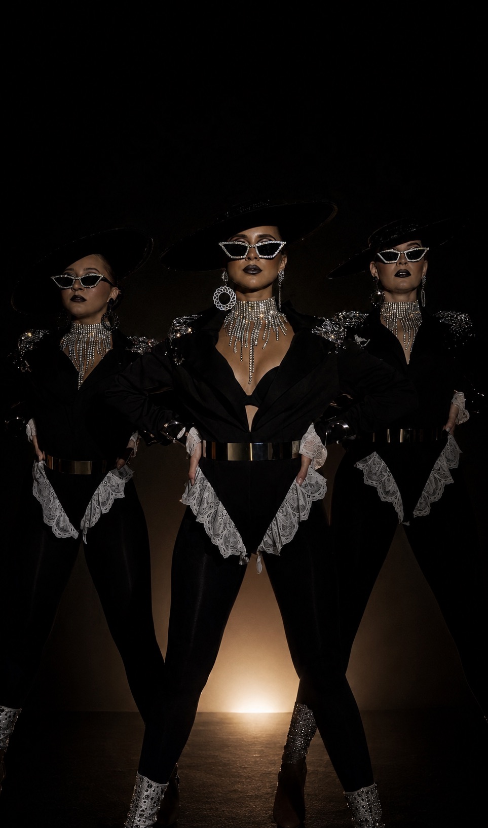 Three performers in black couture with crystal accessories under dramatic stage light